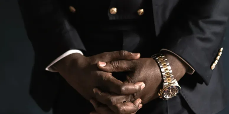 Hands with a gold watch against a dark suit