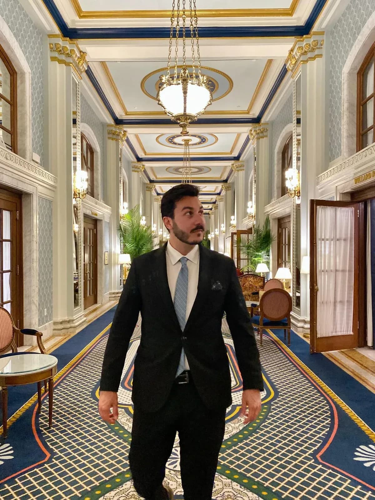 Customer in a black suit walking through an ornate hotel hallway